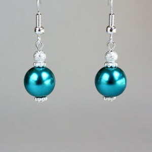 May include: Teal blue pearl drop earrings with silver accents. The earrings have a round pearl bead and a smaller silver bead with a sparkly finish.