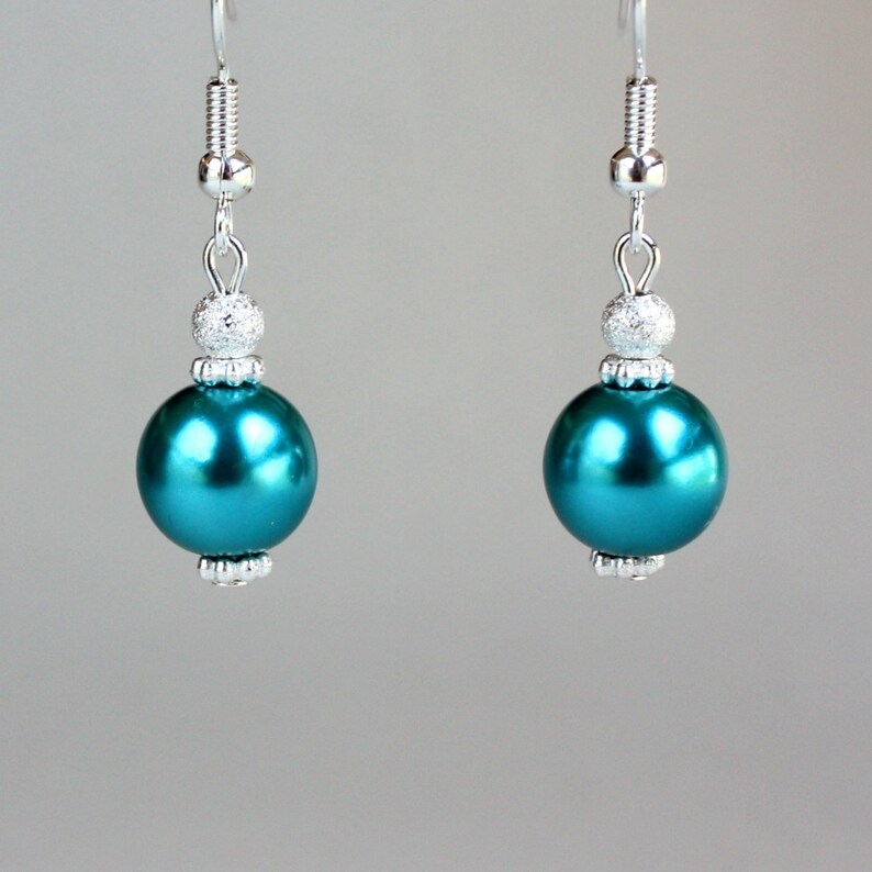 May include: Teal blue pearl drop earrings with silver accents. The earrings have a round pearl bead and a smaller silver bead with a sparkly finish.