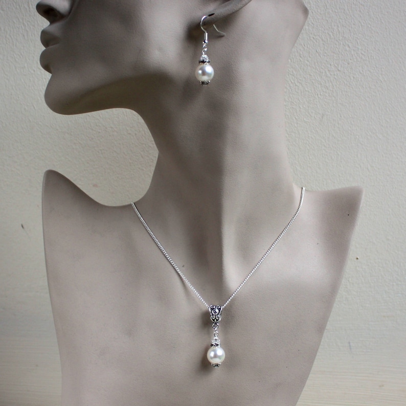 Peut inclure: Un collier et des boucles d'oreilles en argent avec un pendentif en perle blanche et des boucles d'oreilles assorties. Le collier a une cha&icirc;ne d&eacute;licate et un pendentif simple avec un motif floral.
