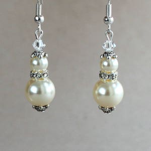 May include: A pair of silver dangle earrings with three white pearls and clear crystal accents.
