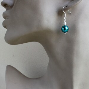 May include: Teal pearl dangle earrings with silver accents. The earrings feature a single large teal pearl bead and smaller white beads on the silver chain.