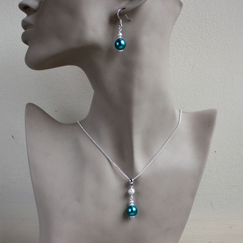 May include: A silver necklace with a teal and white pearl pendant. Matching teal and white pearl earrings are also included.