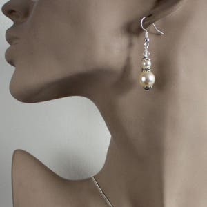 May include: A pair of silver dangle earrings with two white pearl beads and silver accents.