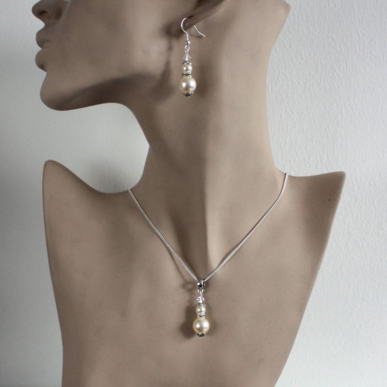 May include: A silver necklace and earrings set featuring a single large pearl and smaller pearl accents. The necklace has a delicate chain and the earrings are drop style.