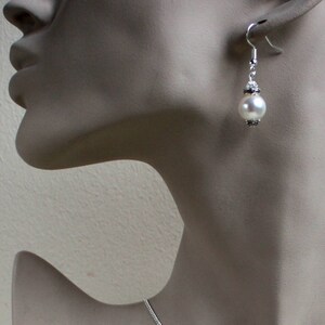 Peut inclure: Boucles d'oreilles pendantes argent&eacute;es avec une perle blanche et des accents argent&eacute;s.
