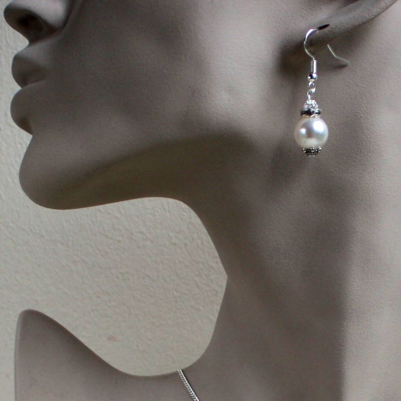Peut inclure: Boucles d'oreilles pendantes argent&eacute;es avec une perle blanche et des accents argent&eacute;s.