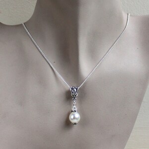 Peut inclure: Un collier en cha&icirc;ne argent avec un pendentif d&eacute;licat orn&eacute; d'une seule perle blanche et de d&eacute;tails argent&eacute;s orn&eacute;s.