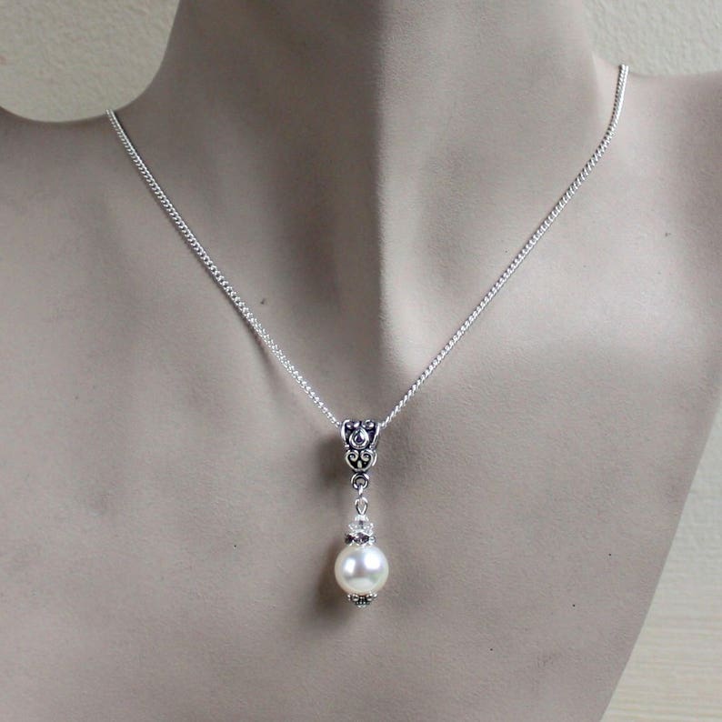Peut inclure: Un collier en cha&icirc;ne argent avec un pendentif d&eacute;licat orn&eacute; d'une seule perle blanche et de d&eacute;tails argent&eacute;s orn&eacute;s.