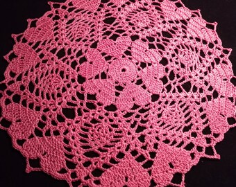 May include: A pink crocheted doily with a delicate floral pattern.
