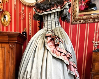 May include: A vintage-style, off-the-shoulder gown with a fitted bodice and a full skirt. The gown is made of a light green fabric with black and pink trim. The skirt has multiple layers of ruffles and lace.