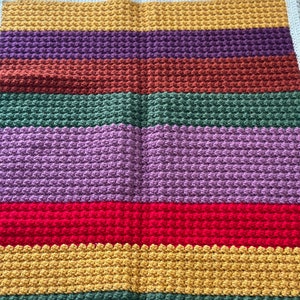 May include: A multi-colored crocheted blanket with stripes of yellow, purple, brown, green, lavender, red, and green. The blanket is made with a textured stitch.