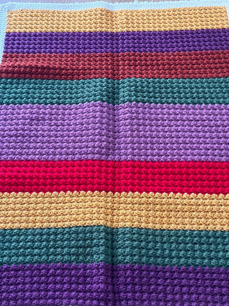 May include: A multi-colored crocheted blanket with stripes of purple, brown, green, red, yellow, and teal.