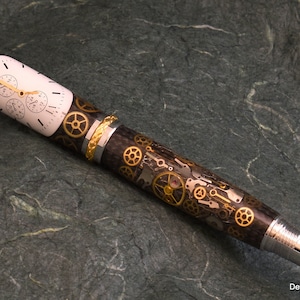 May include: A black and silver pen with a gold band and a watch face design. The pen is decorated with gears and other watch parts.