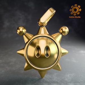 May include: A gold-colored pendant with a sun-like design. The pendant features a smiling face with two oval eyes and a spiky, star-shaped outline. A loop is at the top for a chain. The pendant is likely made of metal.