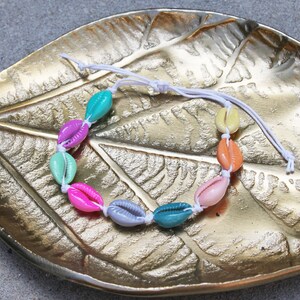 May include: A colorful shell bracelet with a white string. The shells are in a rainbow pattern and are strung on a white cord.
