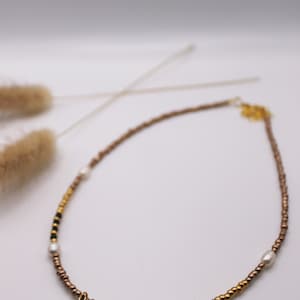 May include: A gold, brown, black, and white beaded necklace with a shell pendant. The shell has a leopard print pattern. The necklace is on a white background.