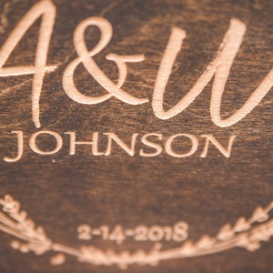 May include: A wooden sign with the text "A&W JOHNSON" and the date "2-14-2018" engraved in a light brown color. The sign is decorated with a floral wreath.