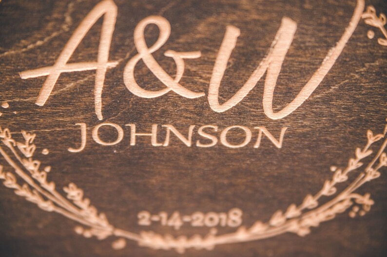 May include: A wooden sign with the text "A&W JOHNSON" and the date "2-14-2018" engraved in a light brown color. The sign is decorated with a floral wreath.