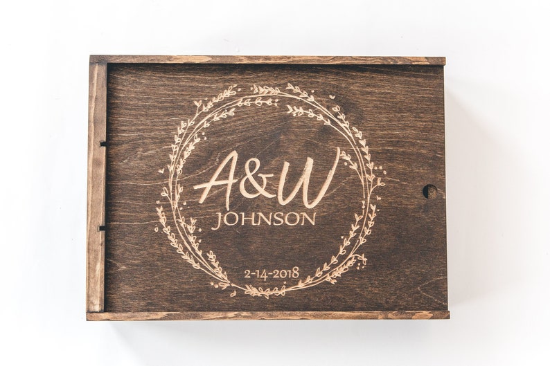 May include: A wooden box with a personalized inscription. The inscription reads "A&W JOHNSON 2-14-2018" and is surrounded by a floral wreath.
