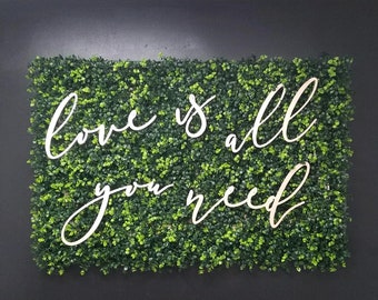 May include: White wooden letters spelling "love is all you need" on a green artificial grass backdrop.