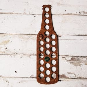May include: Wooden bottle opener shaped like a beer bottle with 30 holes for bottle caps. The bottle opener is brown and has a white background.