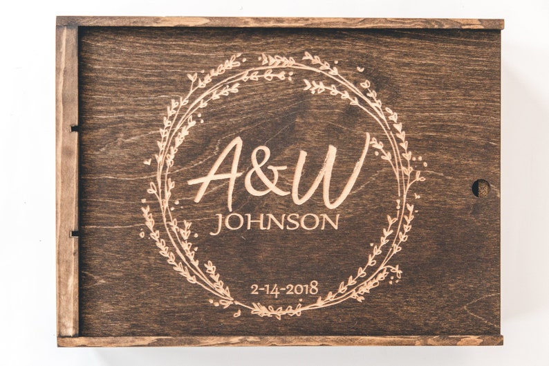 May include: A dark brown wooden box with a hinged lid. The lid is engraved with a floral wreath design and the text "A&W JOHNSON 2-14-2018".