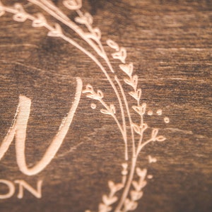 May include: A close-up of a wooden sign with a floral wreath design and the word "Love" engraved in the center.