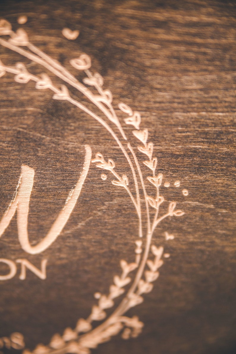May include: A close-up of a wooden sign with a floral wreath design and the word "Love" engraved in the center.
