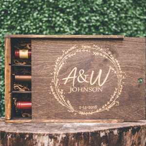 May include: A wooden box with a sliding lid, engraved with a floral wreath, the initials "A&W" and the name "JOHNSON" and the date "2-14-2018". The box contains three small bottles of wine.