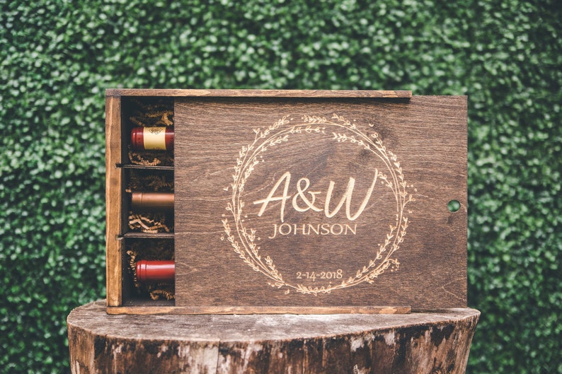 May include: A wooden box with a sliding lid, engraved with a floral wreath, the initials "A&W" and the name "JOHNSON" and the date "2-14-2018". The box contains three small bottles of wine.