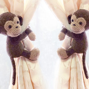 May include: Two brown crocheted monkey curtain tiebacks with long tails hanging from a pair of cream coloured curtains.
