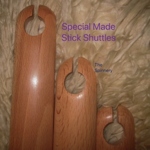 May include: Three wooden stick shuttles of varying sizes, with a rounded shape and a hole in the center. The shuttles are made of light brown wood and are arranged in a row from largest to smallest. The text "Special Made Stick Shuttles" and "The Spinnery" is visible in the image.