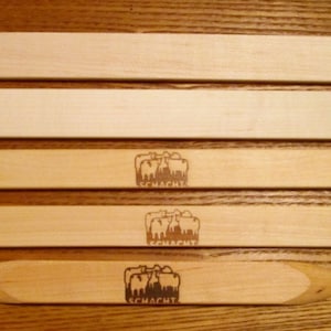 May include: Five wooden knitting needles of varying lengths. The needles are all made of natural wood and have a smooth finish. The needles are labeled with the word "Schmacht" in a stylized font.