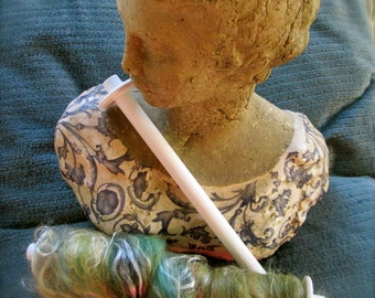 May include: A white ceramic bust with a blue and white floral pattern, a white spindle, and a skein of green, blue, and white yarn.