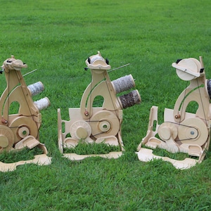 May include: Three wooden spinning wheels with yarn spools on a grassy lawn. The wheels are made of light wood and have a natural finish. The yarn spools are various colors and textures.