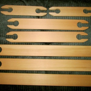 May include: Set of six wooden weaving heddles, with two shorter heddles and four longer heddles. The heddles are made of natural wood and have a smooth finish.