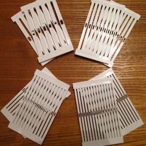 May include: Five white plastic weaving looms, each with multiple rows of evenly spaced holes. The looms are arranged in a circular pattern on a wooden surface.