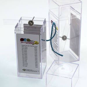 May include: A clear plastic box with a label that reads "Yarn to Yards Balance" and lists the typical yarn types and yards per pound. The box is open and a blue yarn is threaded through the top.