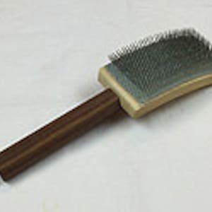 May include: A wooden pet grooming brush with a dark brown handle and a rectangular brush head with metal bristles. The brush head is attached to a light-colored wooden base. The brush is designed for grooming pets.