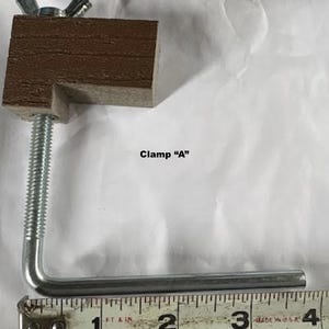 May include: A metal and wood clamp with the text "Clamp A". The clamp has a brown wooden block, a threaded rod, and a metal bar. The ruler shows the clamp is about 4 inches long.