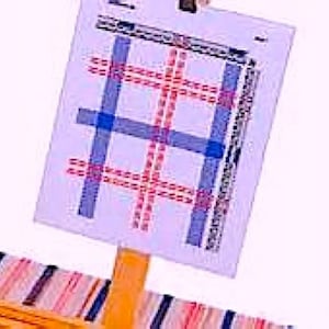 May include: A small wooden easel with a white canvas featuring a blue and red plaid pattern. The easel is made of wood and has a natural finish.