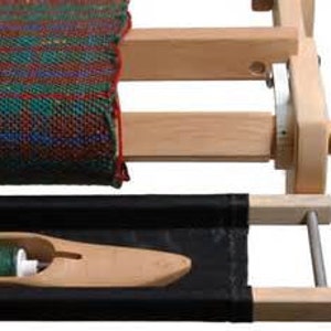 May include: A wooden loom with a partially woven green, red, and blue plaid fabric on the warp. A wooden shuttle with a green yarn bobbin is in the bottom right corner.