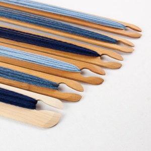 May include: A set of wooden weaving needles with blue and light blue yarn wound around them. The needles are arranged in a row, with the yarn extending out from the ends.