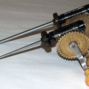 May include: A vintage hand-cranked drill with two metal drill bits and a brass gear with the text "AUG. SCHMIDT & SOHN WIESBADEN" printed on it.