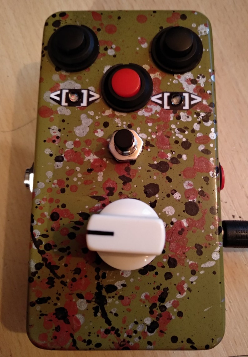 May include: A green, red, and black guitar effects pedal with a white knob, two black buttons, and a red button. The pedal has a splatter paint design.