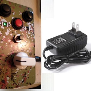 May include: A green and white splatter-painted guitar effects pedal with three knobs, a red button, and a white toggle switch. The pedal is connected to a black power adapter with a US plug.