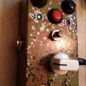 May include: A green and black speckled guitar effects pedal with three knobs, two buttons, a toggle switch, and a white knob. The pedal has a green LED light that is on.