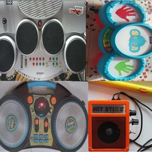 May include: A set of four toy musical instruments, including a drum set, a toy keyboard, a set of three hand-held drums, and a small amplifier with the text "HIT STIX 2".
