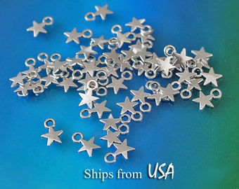 May include: A pile of silver star-shaped charms with a jump ring on each star. The charms are scattered on a blue background.