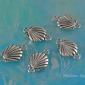May include: Five silver-toned metal shell-shaped charms with two jump rings each. The charms are on a light blue background.